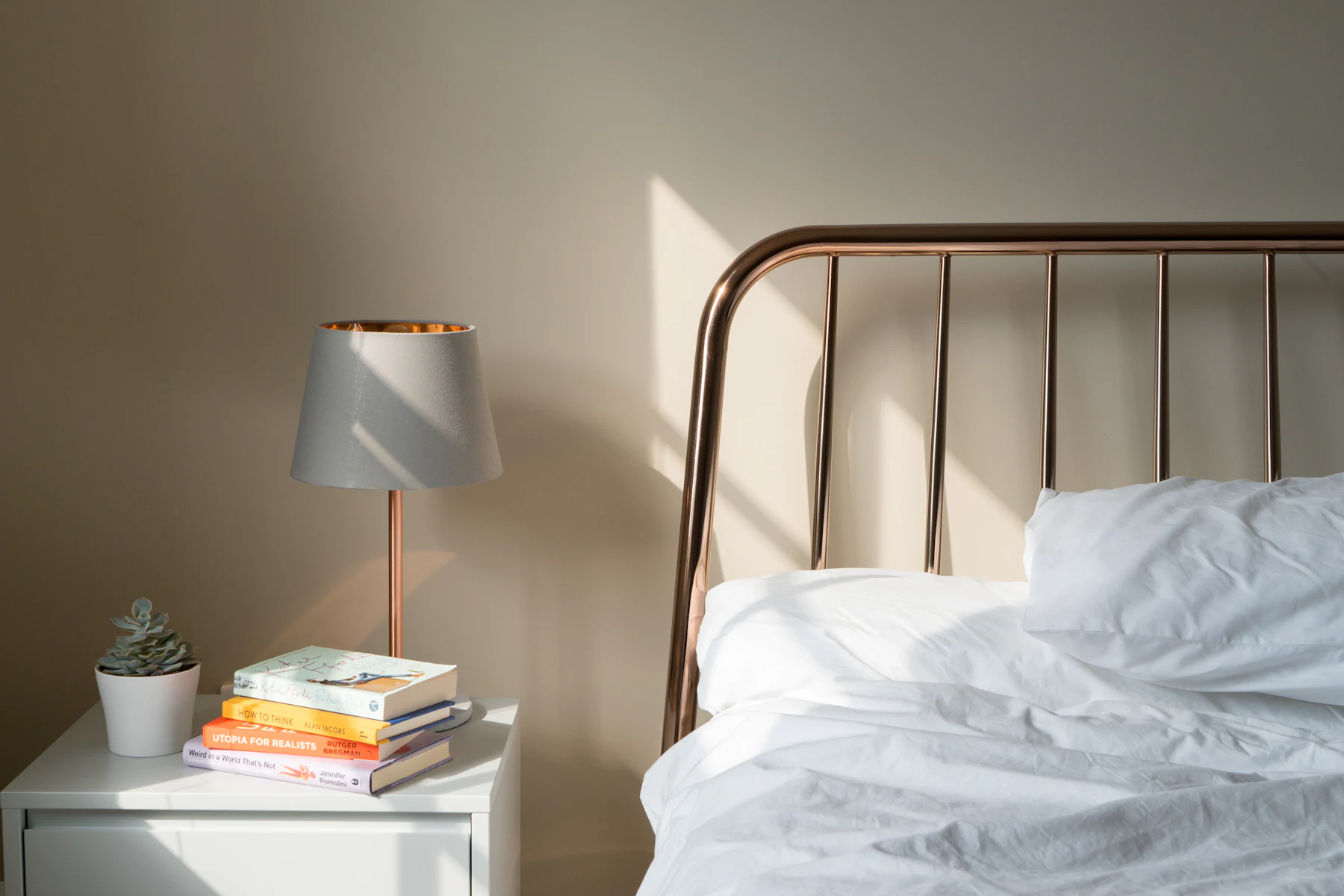 A made bed with white linen beside a lamp on a bedside table